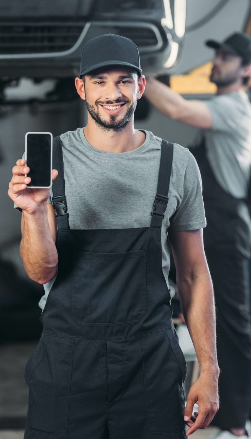 professional-mechanic-showing-smartphone-with-blank-screen-while-colleague-working-in-workshop.jpg